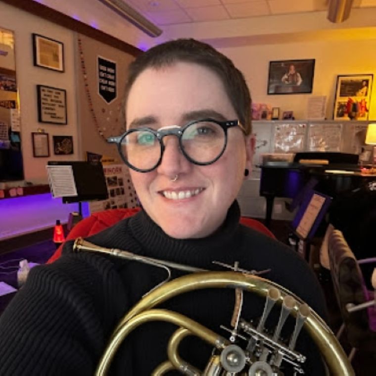 Picture of Maddy Tarantelli taking a selfie in office, holding horn