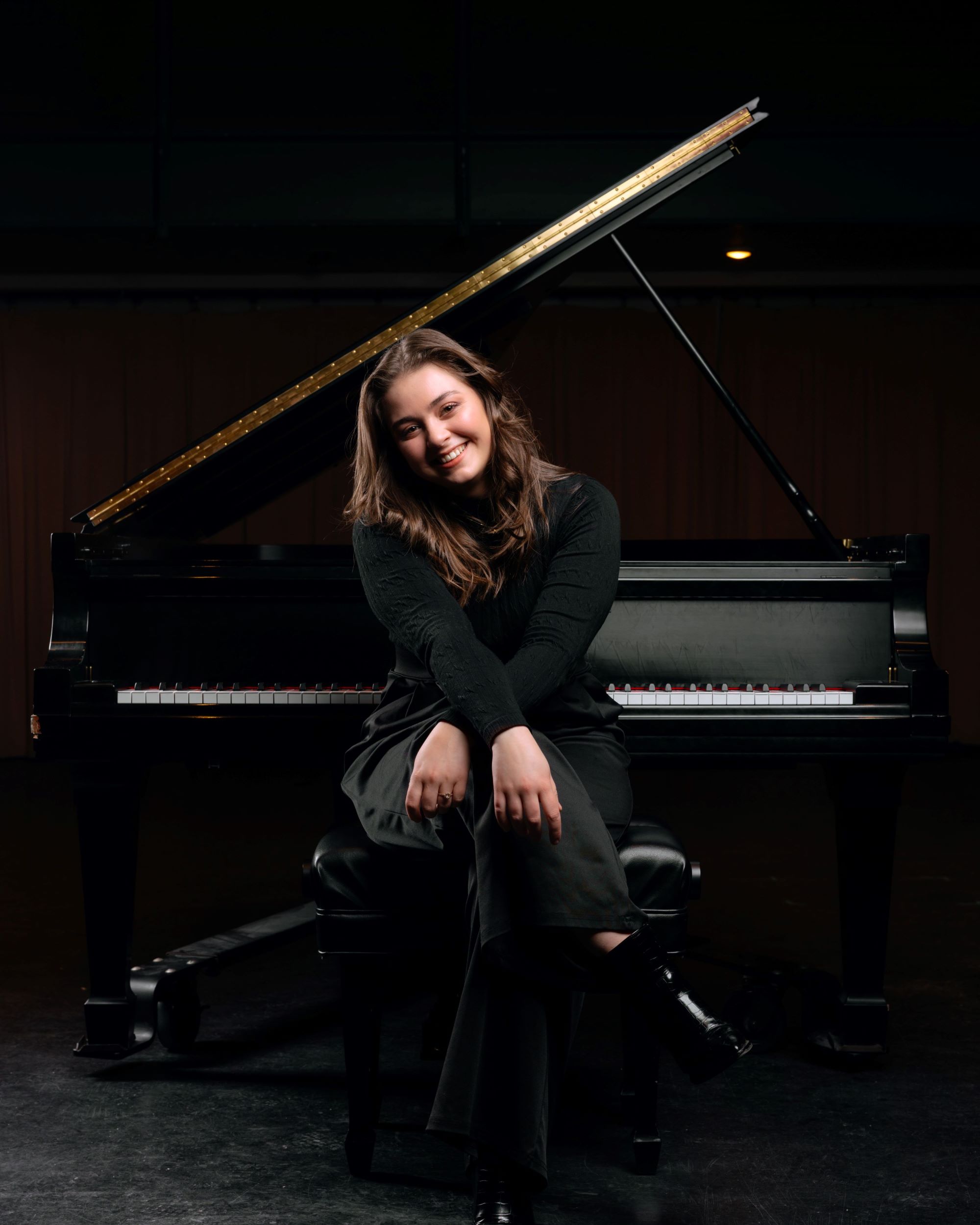 Madelyn Potter sitting in front of grand piano, facing away from the keyboard