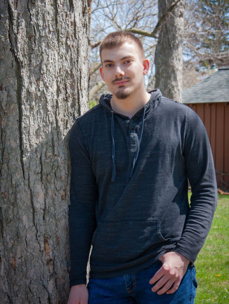Adam Schroeder standing, learning against tree
