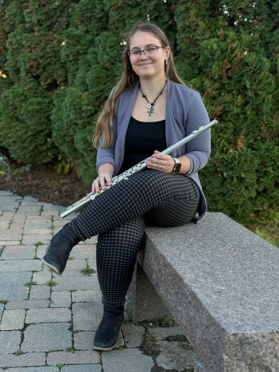 Ashlynn sitting outside on a concrete bench, legs crossed, holding a flute