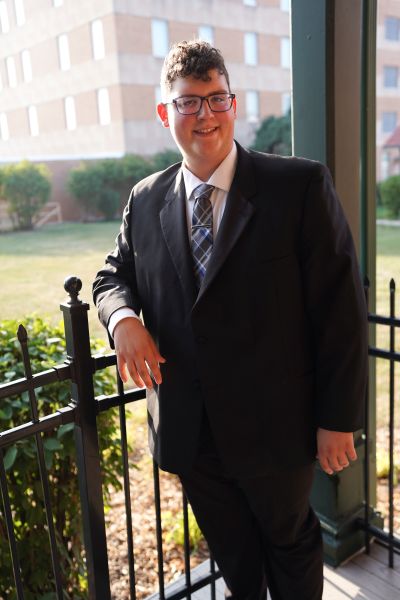 Zach Midtling wearing a suit, leaning against a patio fence, outside.