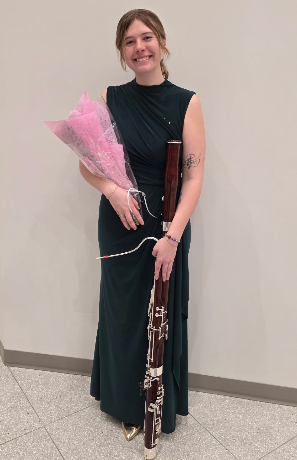 Kate VanGorp standing, holding bassoon and bouquet of flowers.
