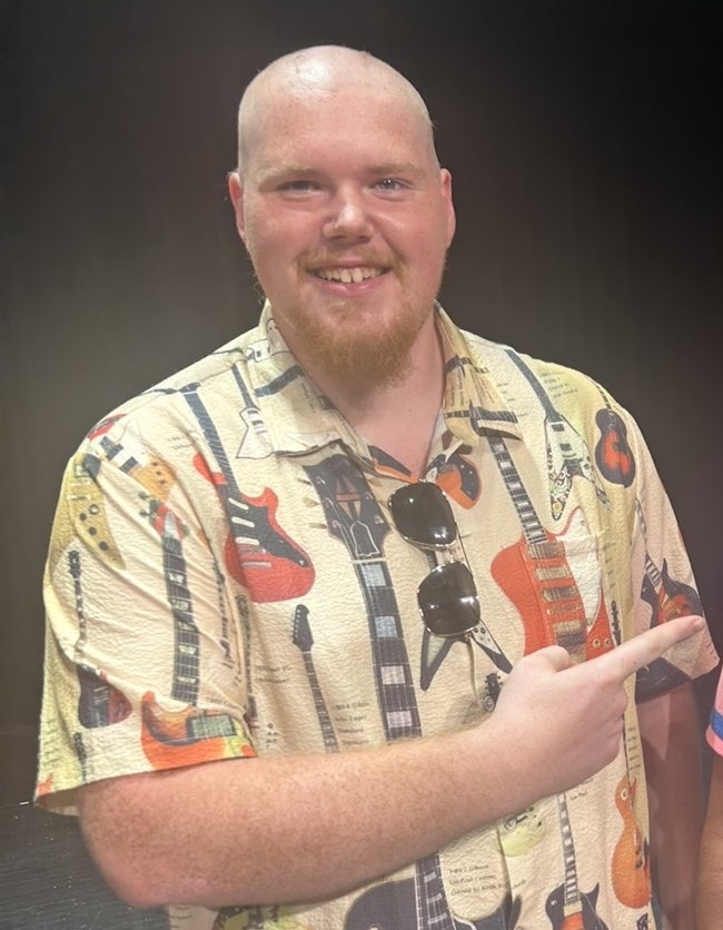 Logan Lubahn standing and smiling, pointing to something at the side.