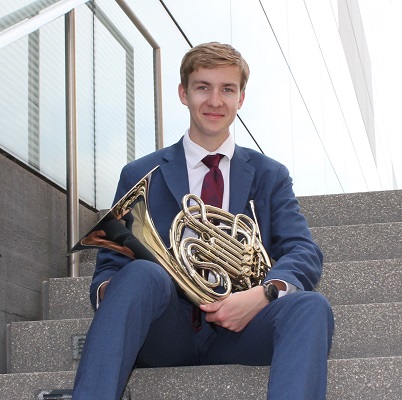 Patrick Mooney holding french horn and sitting on stairs