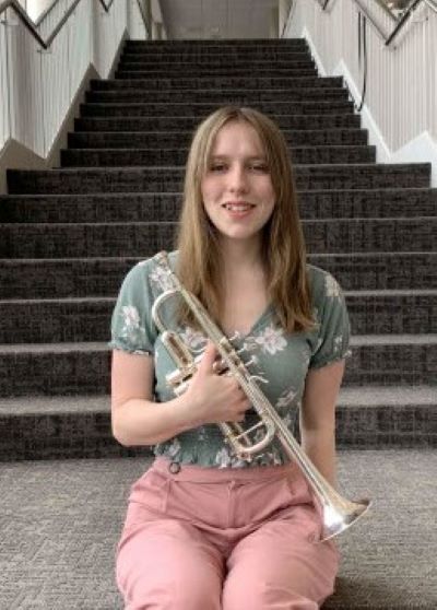 Megan Bennett holding trumpet while sitting on stairs