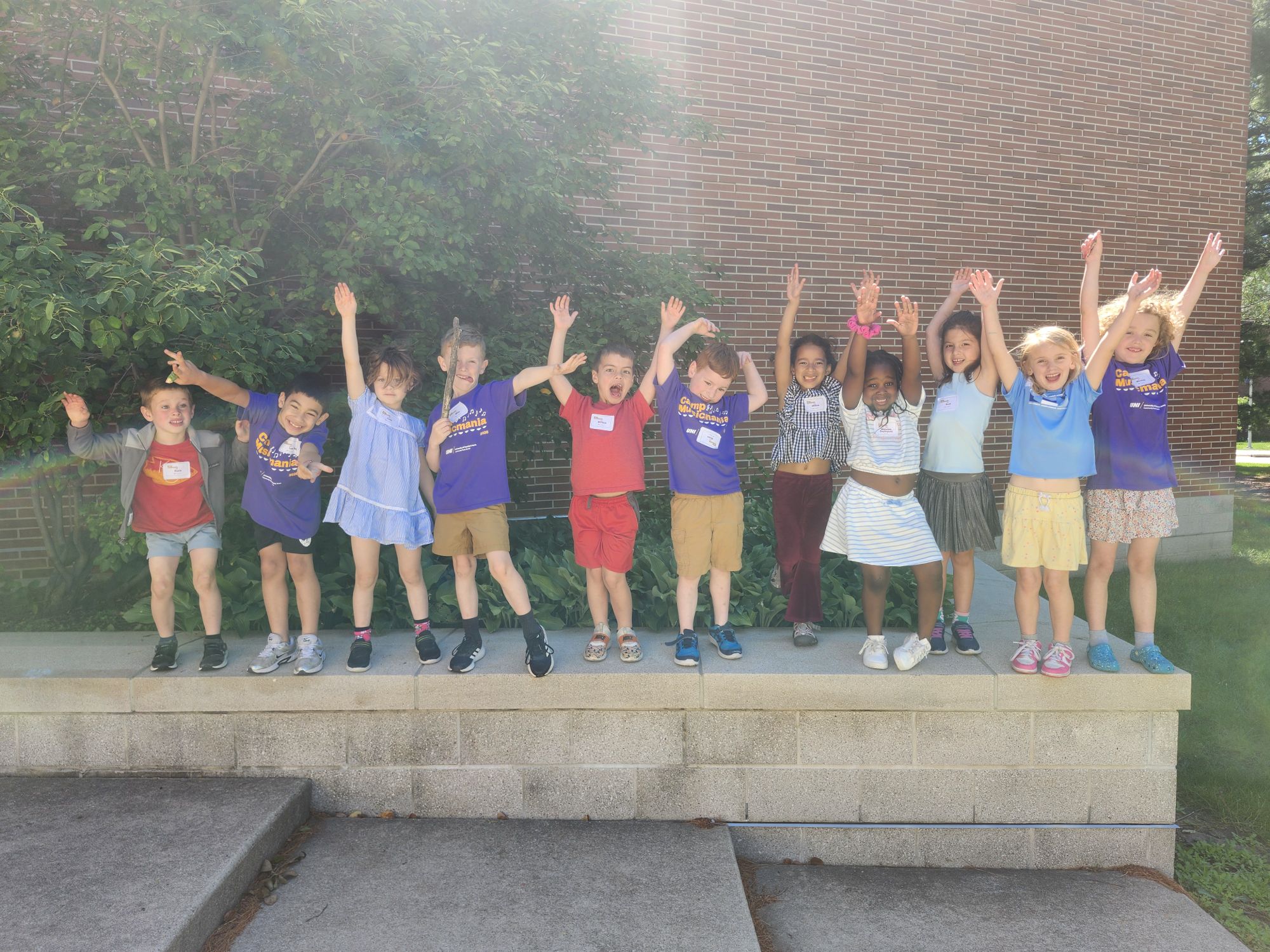 Group of kids standing in a straight line, waving their hands in the air