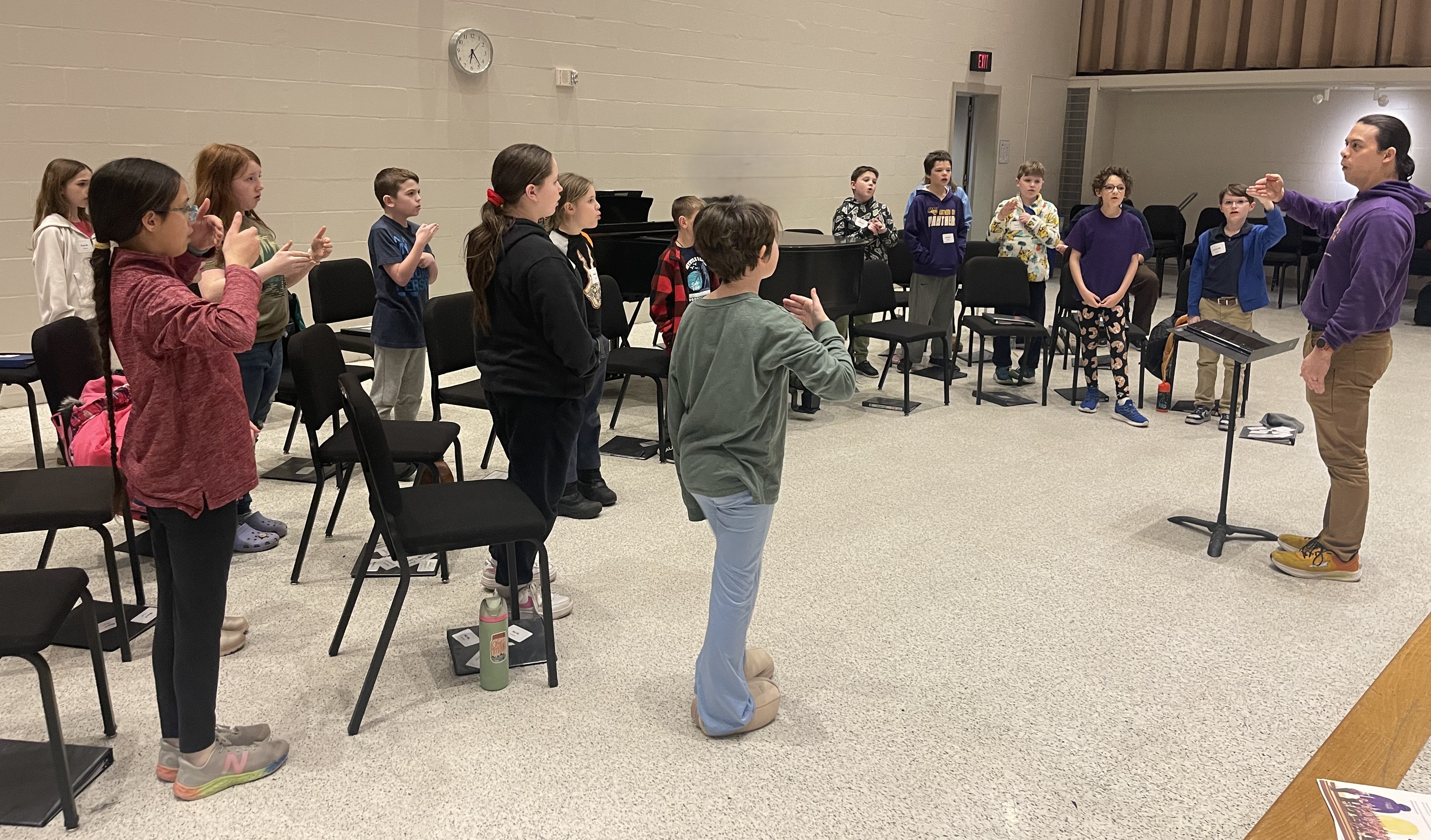 Kids standing in a half circle around a director who is showing solfege movements.