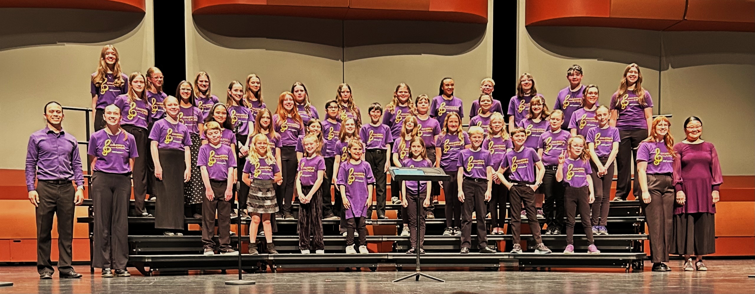 Group picture of UNI Children's Choir with staff after a concert, standing on risers.