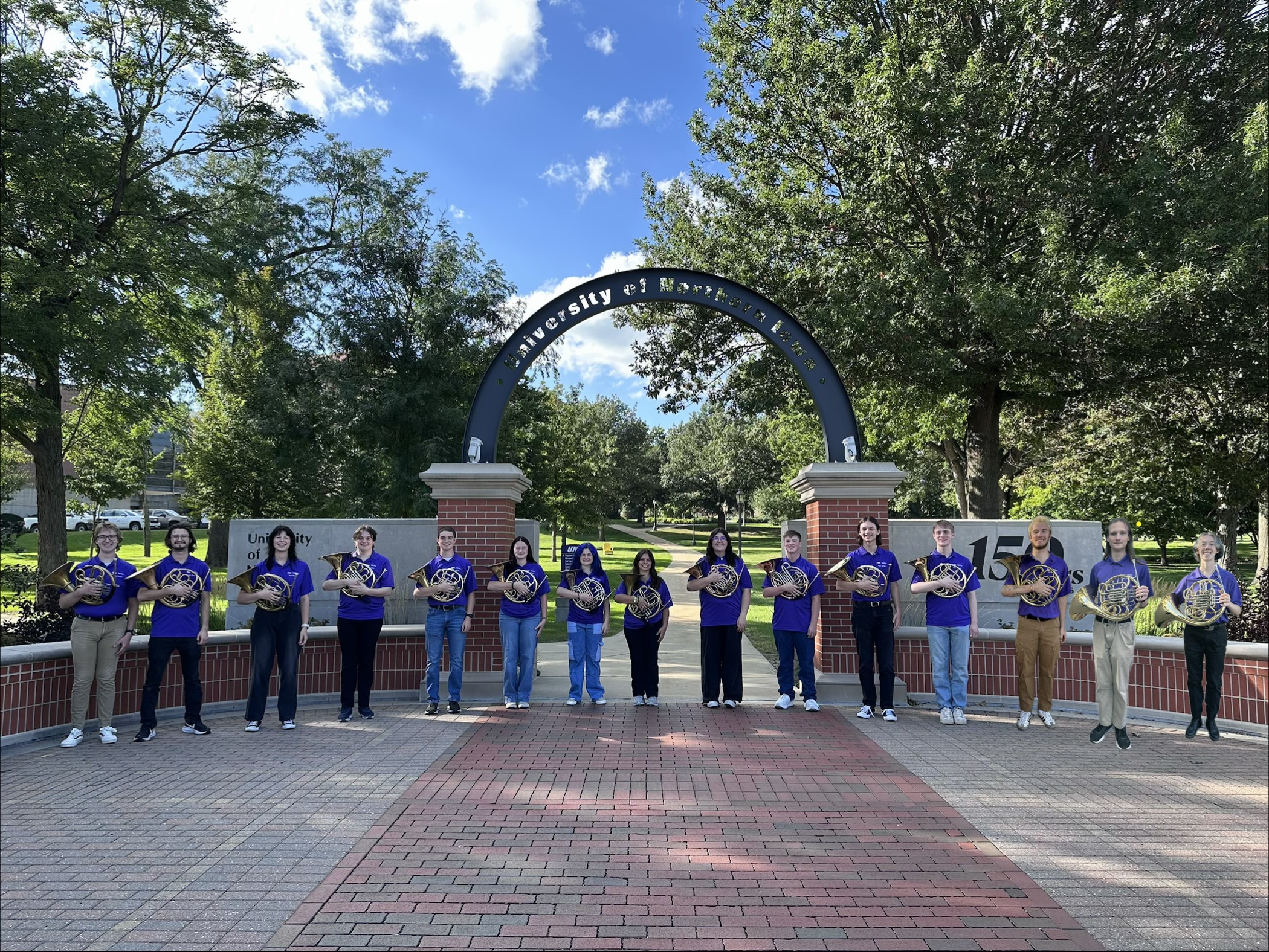 15 horn students pose with their instruments under the University of Northern Iowa arch