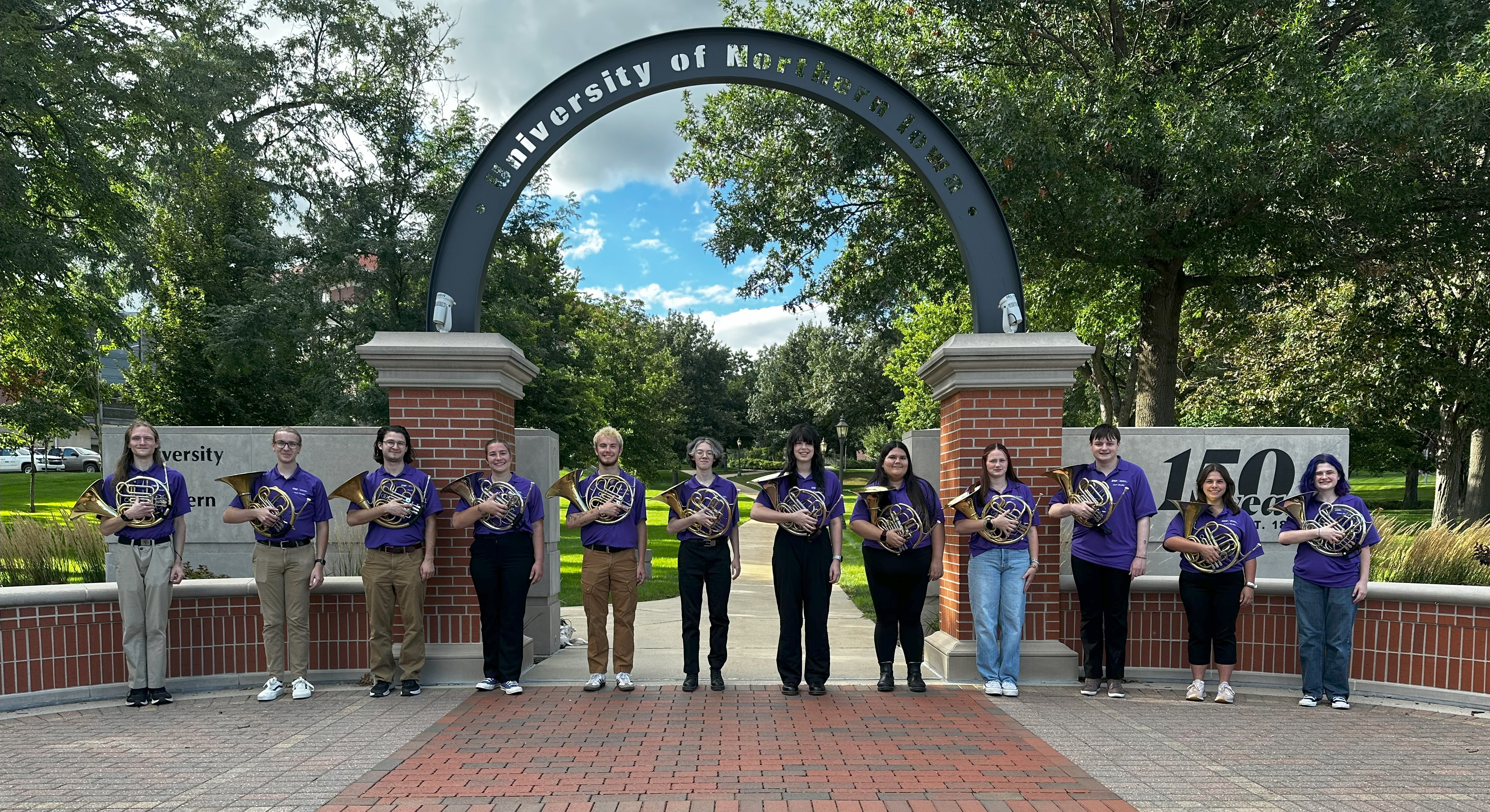 12 horn students pose with their instruments under the University of Northern Iowa arch