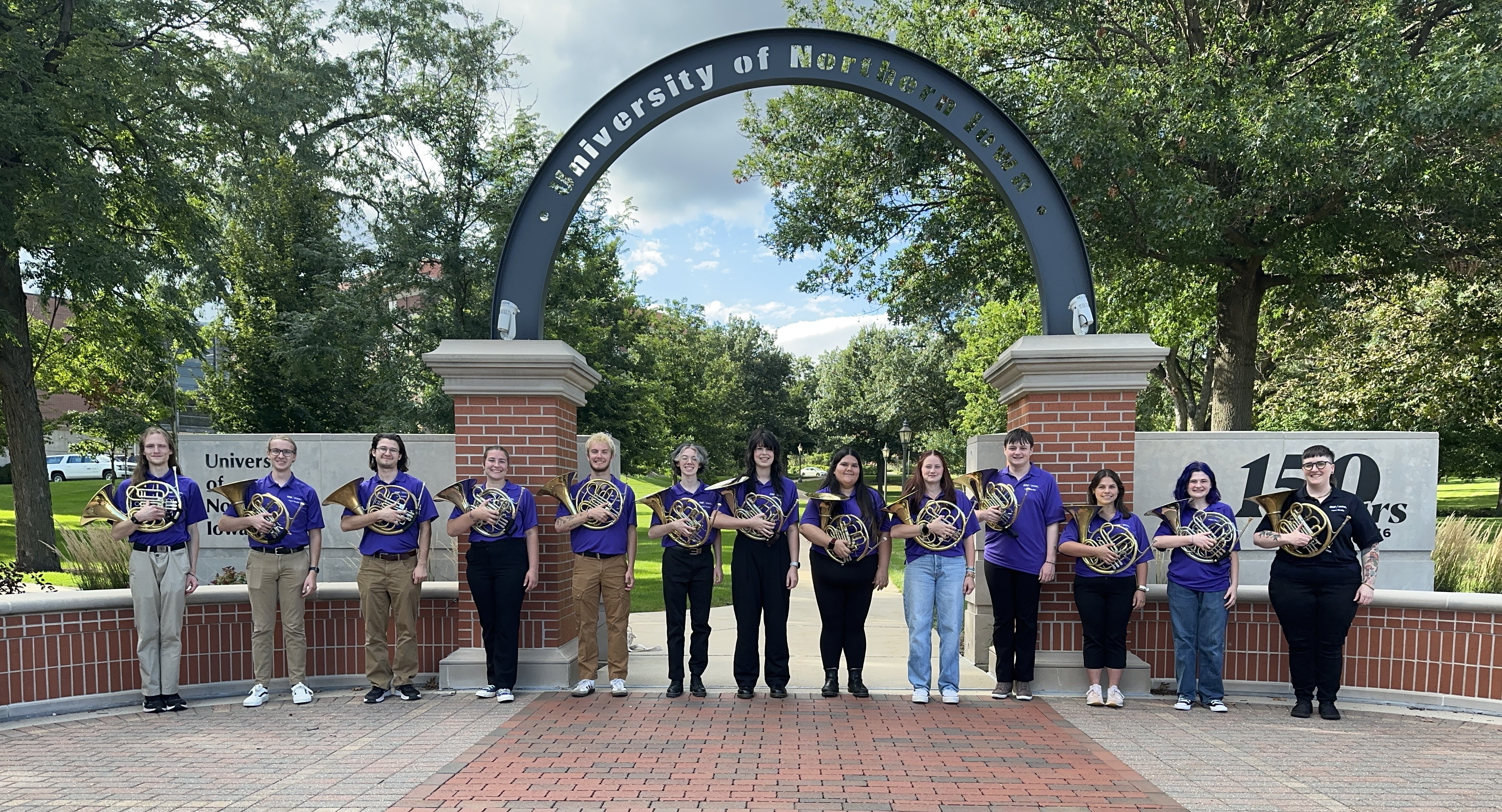 Horn students and professor pose with horns under UNI arch 