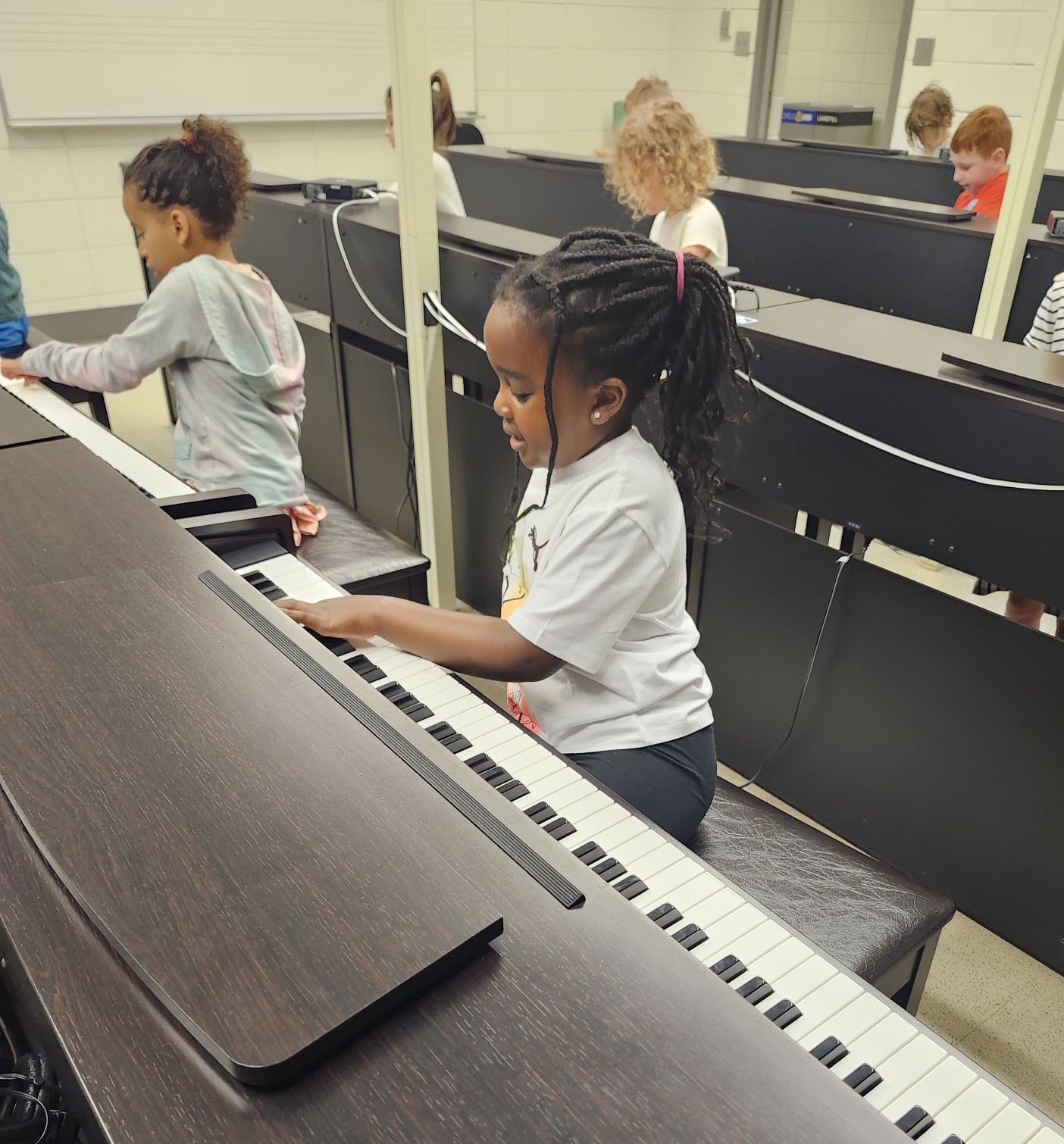 two girls playing pianos in a group piano lab