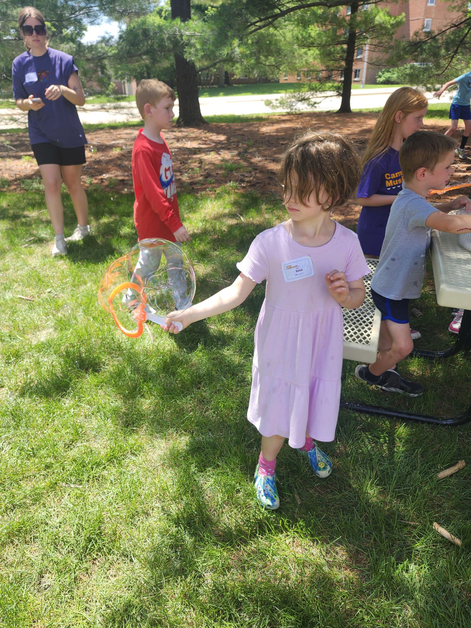 kids outside playing with bubbles. a girl at the front using a bubble wand