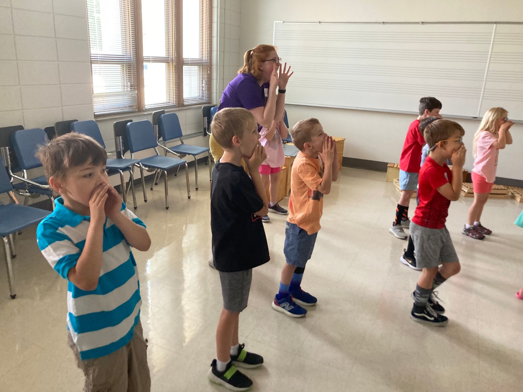kids standing in lines, in a classroom, holding their hands around their mouth, with dance movements.