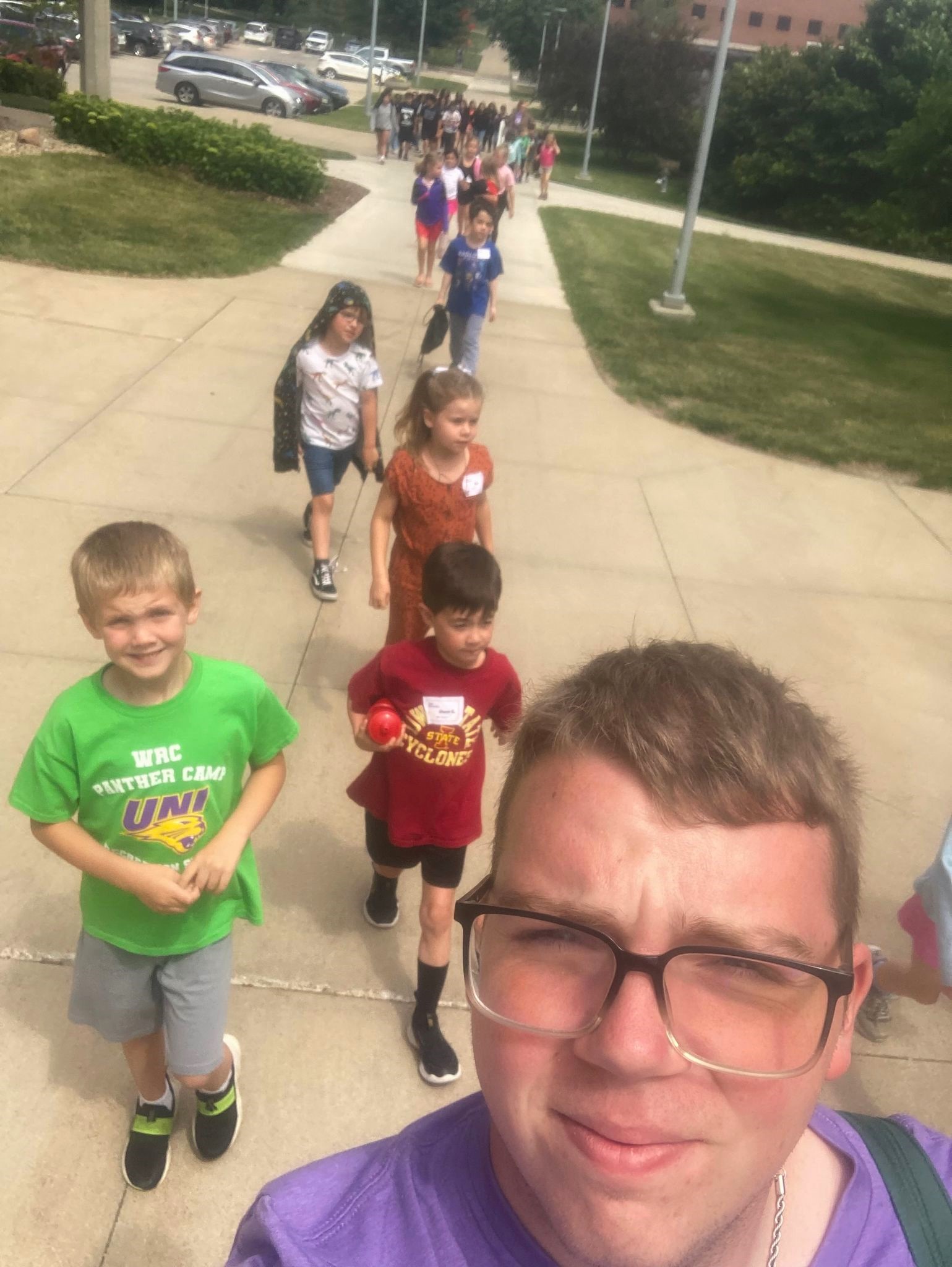 Group of students walking behind teacher outside.