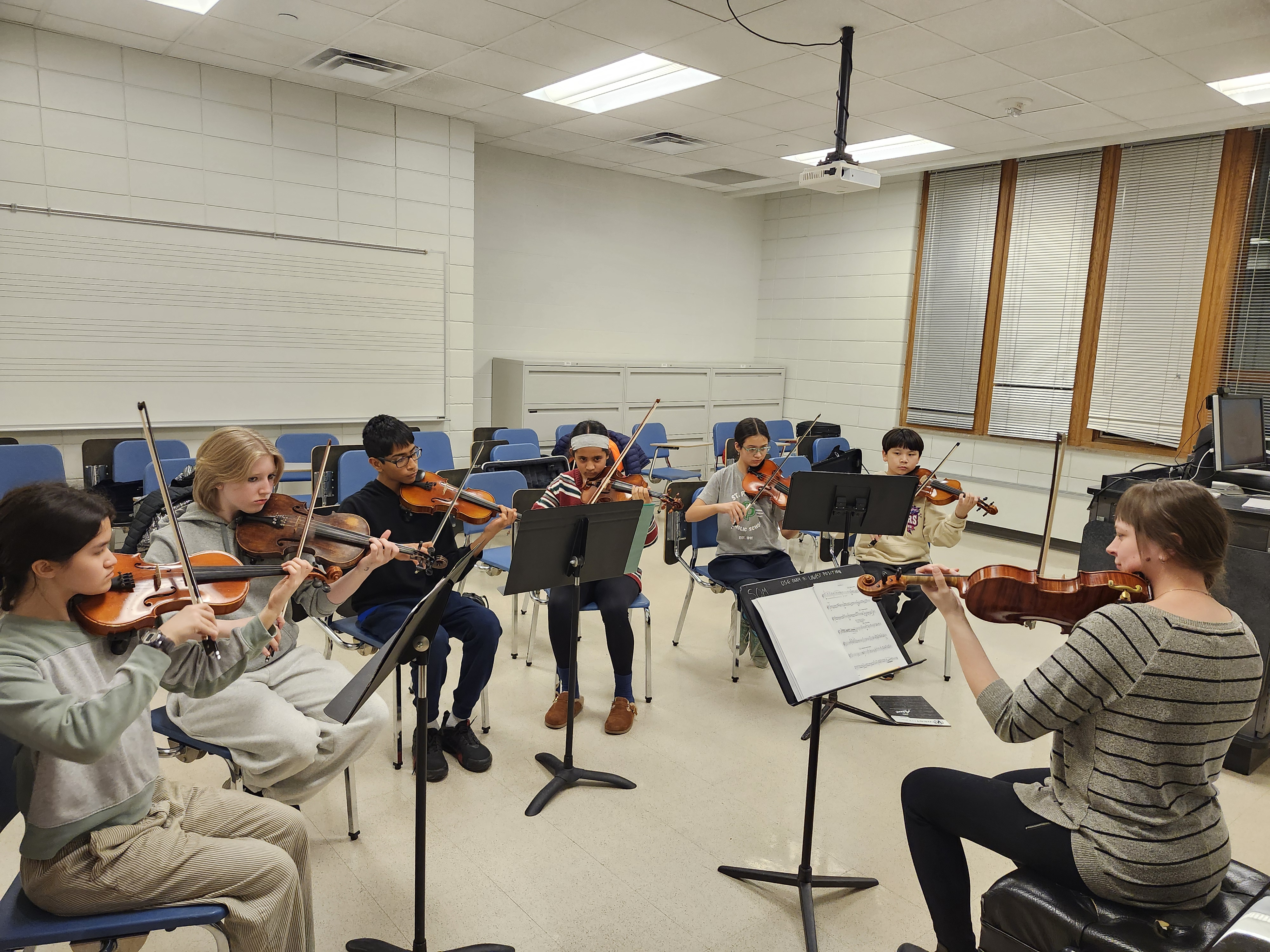 a group of middle school violinists in sectional with their teacher