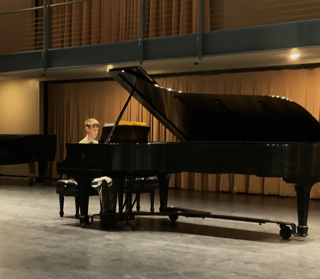Student performing on grand piano during a recital.