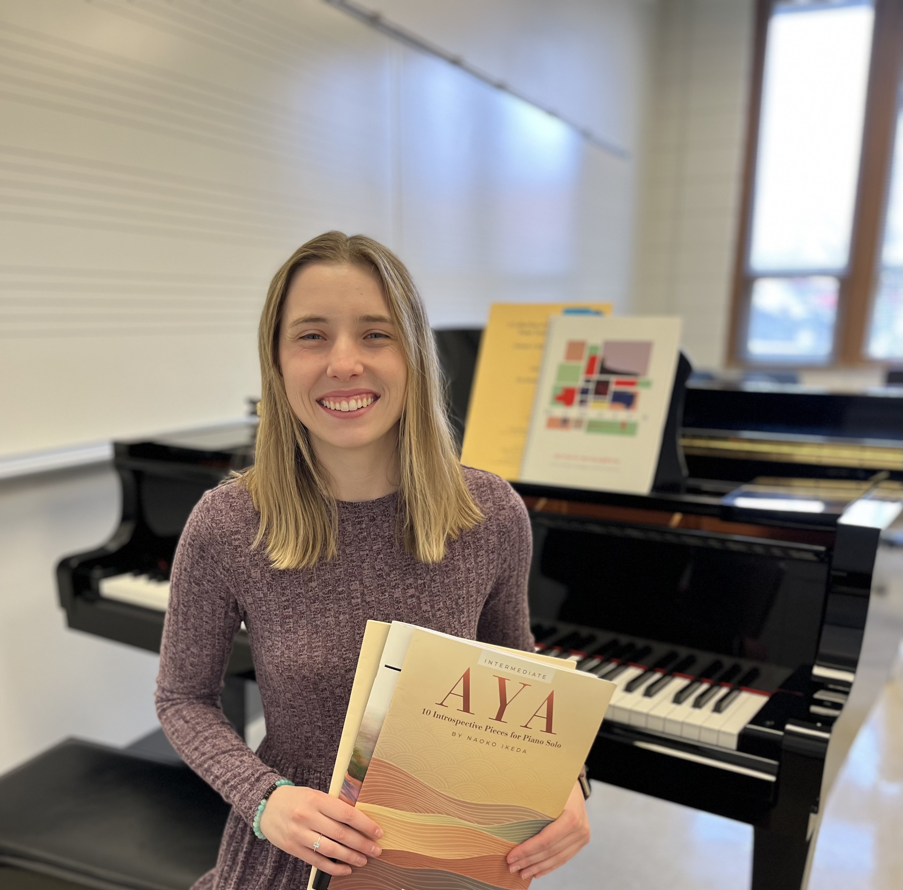 Morgan List sitting at a piano, smiling and holding piano books