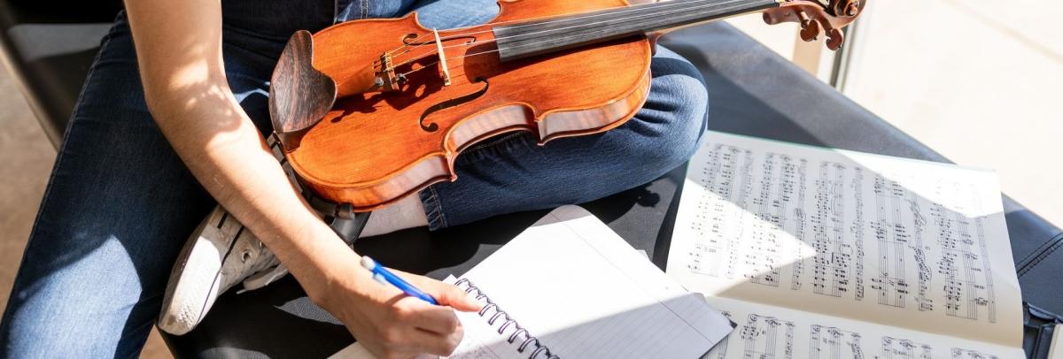a student writes in a notebook as they hold a violin