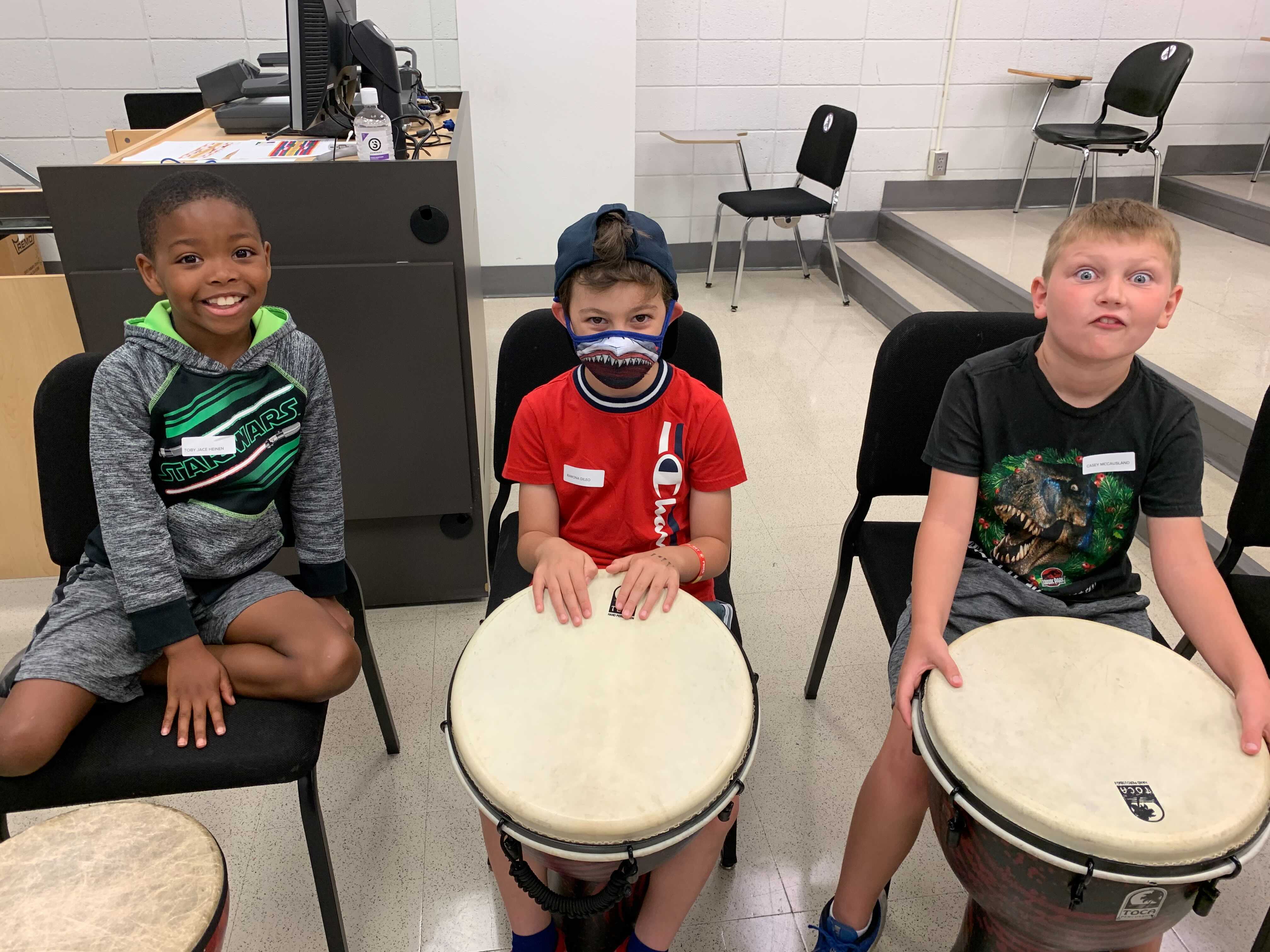 Three boys sitting behind drums