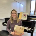 Morgan List sitting at a grand piano, facing away from the piano, holding music books.