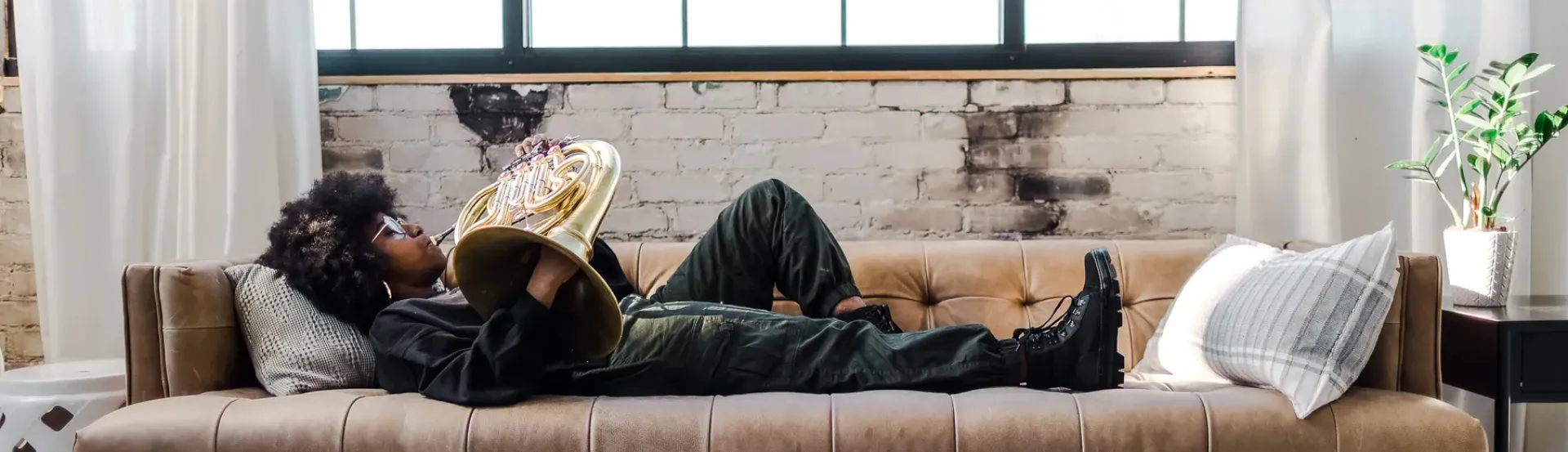 Photo of guest artist Aliyah Danielle lying on her back on a couch, playing horn